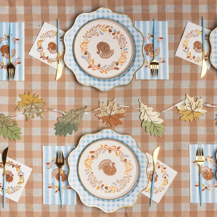 Thanksgiving table setting with decorative plates, napkins, and cutlery on a checkered tablecloth.