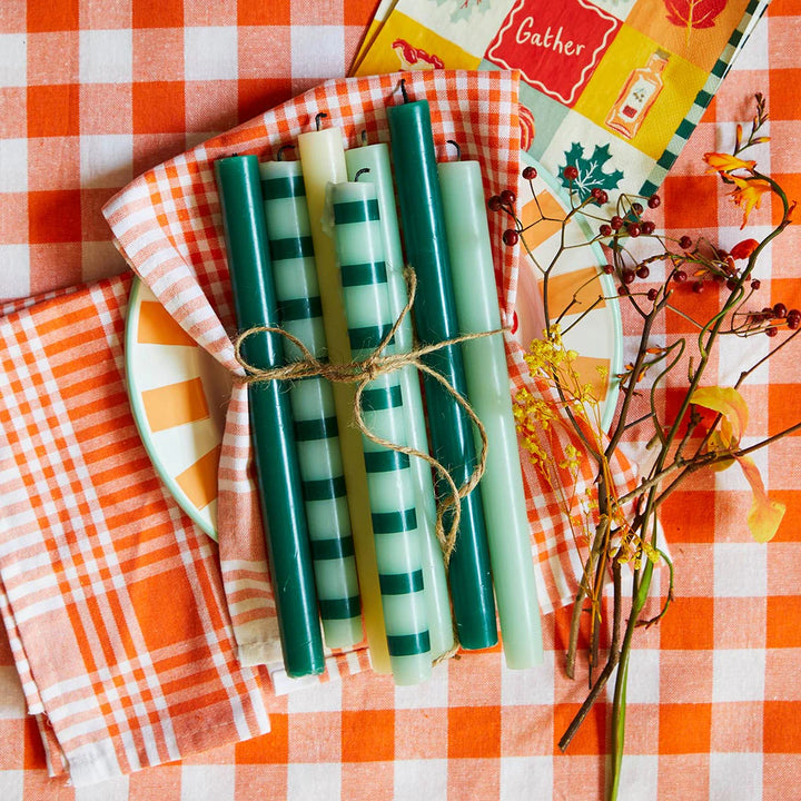 Set of green and white candles tied with twine on a checkered tablecloth with decorative elements.