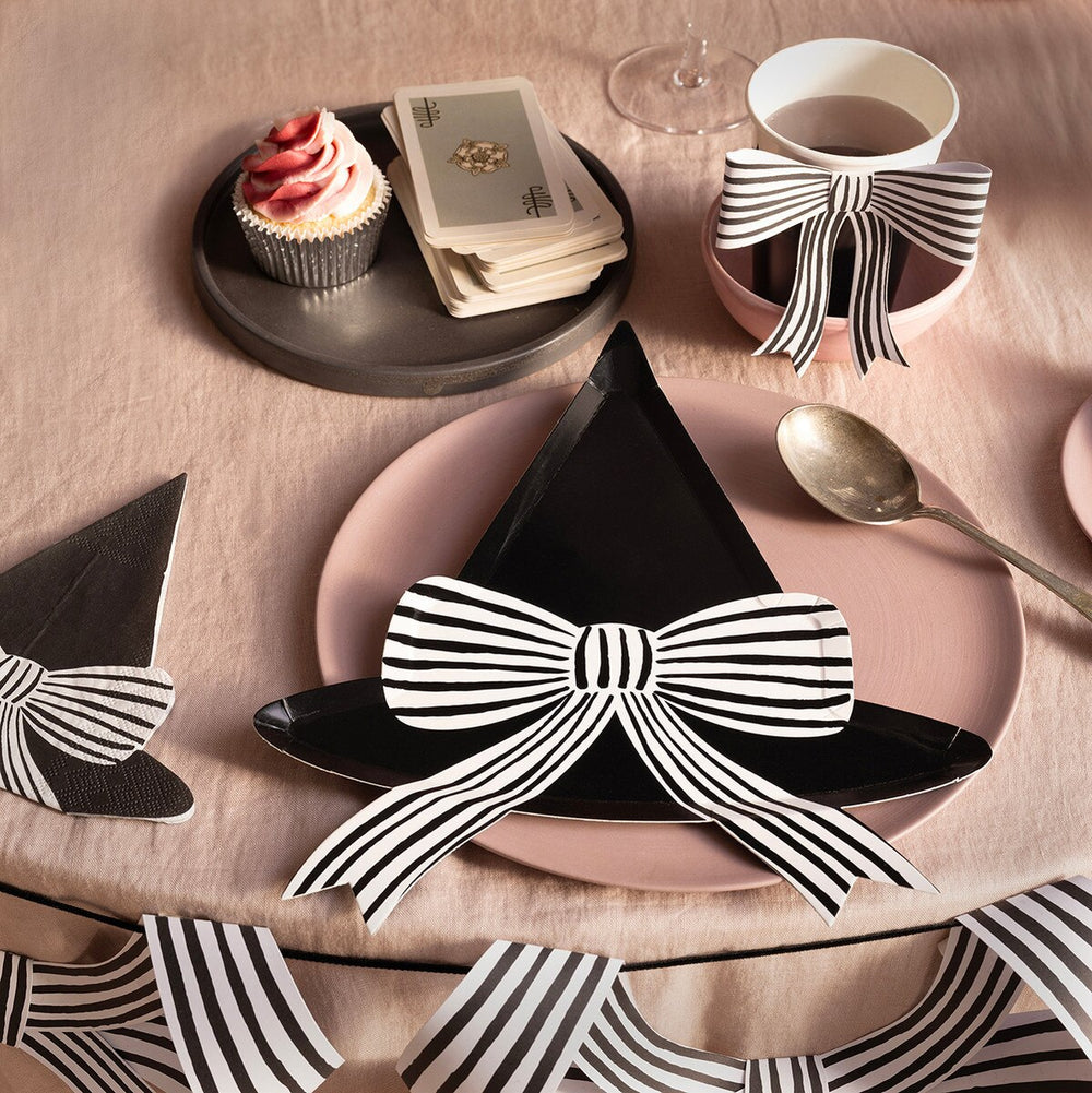 Table setting with black and white striped bow decorations on a pink tablecloth.